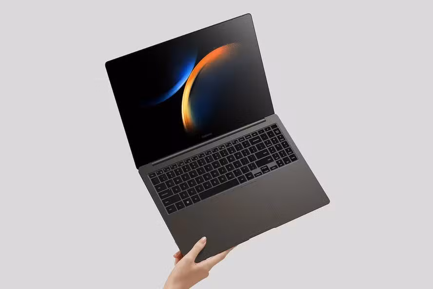 Mão segurando um laptop Galaxy Book3 Ultra em um fundo cinza.