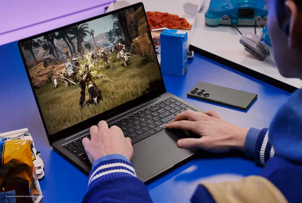 Mão em um laptop sobe uma mesa azul com um smartphone ao lado.