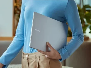 Homem de camisa azul segurando um laptop Galaxy Book4. Pro