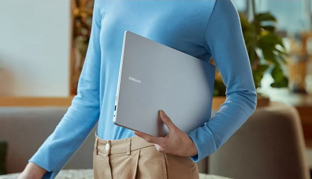 Homem de camisa azul segurando um laptop Galaxy Book4. Pro