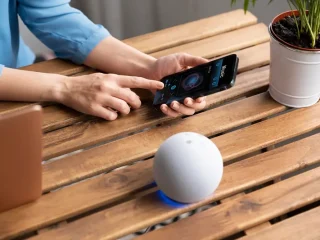 Assistente Virtual sobre uma mesa de madeira com uma mulher mexendo no smartphone.