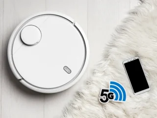 Robô aspirador cor branco ao lado de um tapete cor branco e um smartphone.