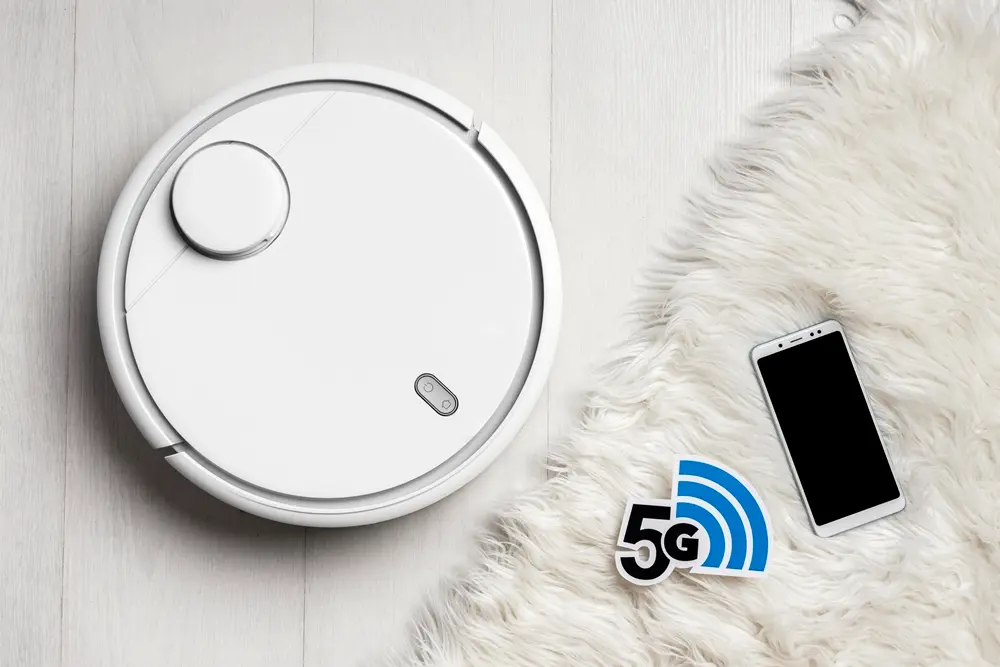 Robô aspirador cor branco ao lado de um tapete cor branco e um smartphone.