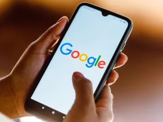 Mãos segurando um smartphone exibindo a tela do buscador Google