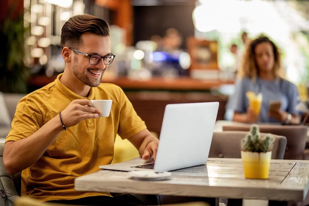 Homem sentando em uma mesa tomando uma xicara de café olhando para tela de um notebook. ChatGPT