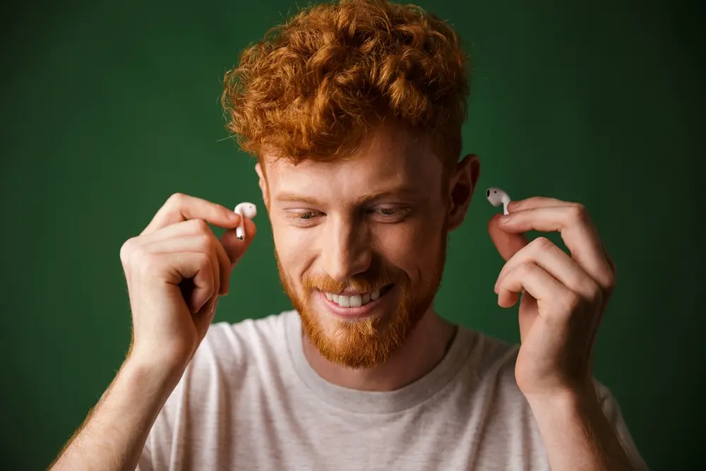 Uma pessoa colocando fones de ouvido Bluetooth em um fundo verde.