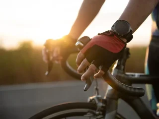 Braço de um homem segurando o guidão de uma bike de estrada usando luvas de ciclismo e um smartwtch. Smartwatch para ciclismo com GPS