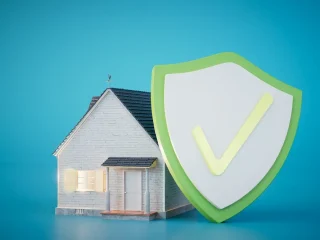 Uma pequena casa ao lado de um grande escudo verde e branco com uma marca de seleção, simbolizando proteção e segurança do lar.