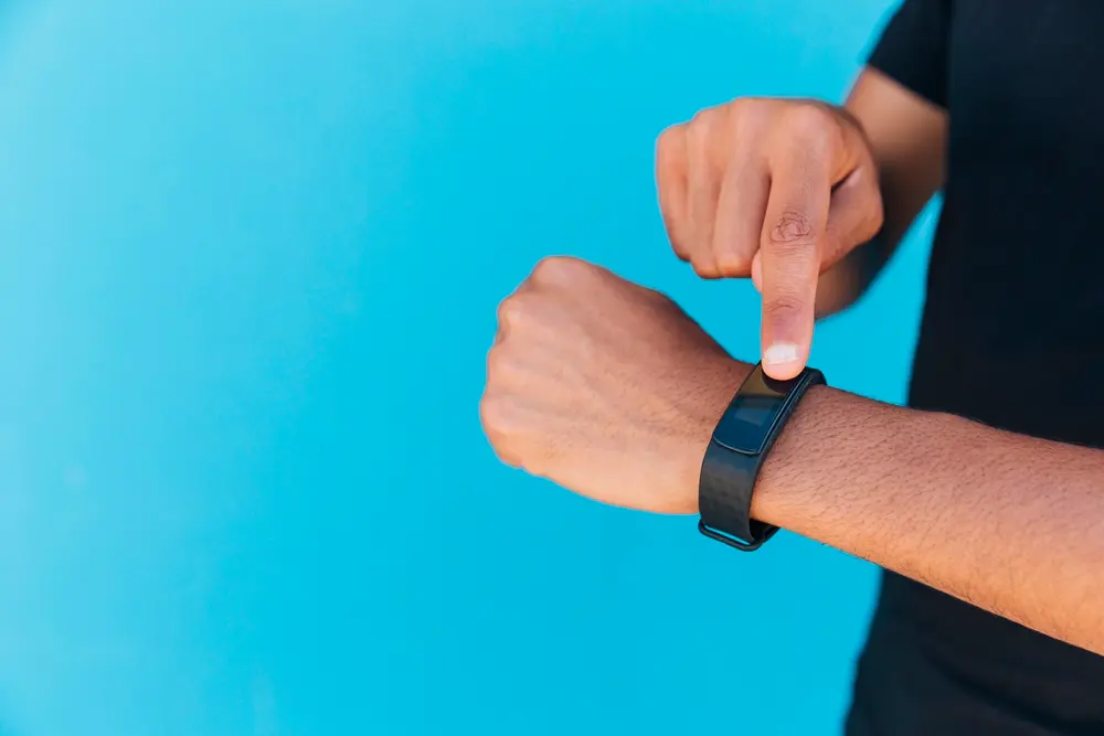 Braço masculino exibindo uma smartband no pulso esquerdo em um fundo azul.