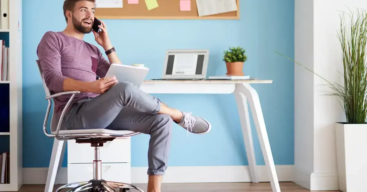 Uma pessoa sentada confortavelmente em um home office, segurando um tablet e falando ao telefone, cercada por uma decoração elegante.