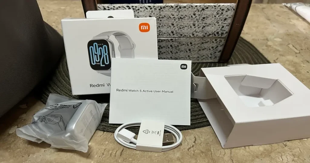 Redmi Watch 5 Active fora da caixa e acessórios sobre a mesa.