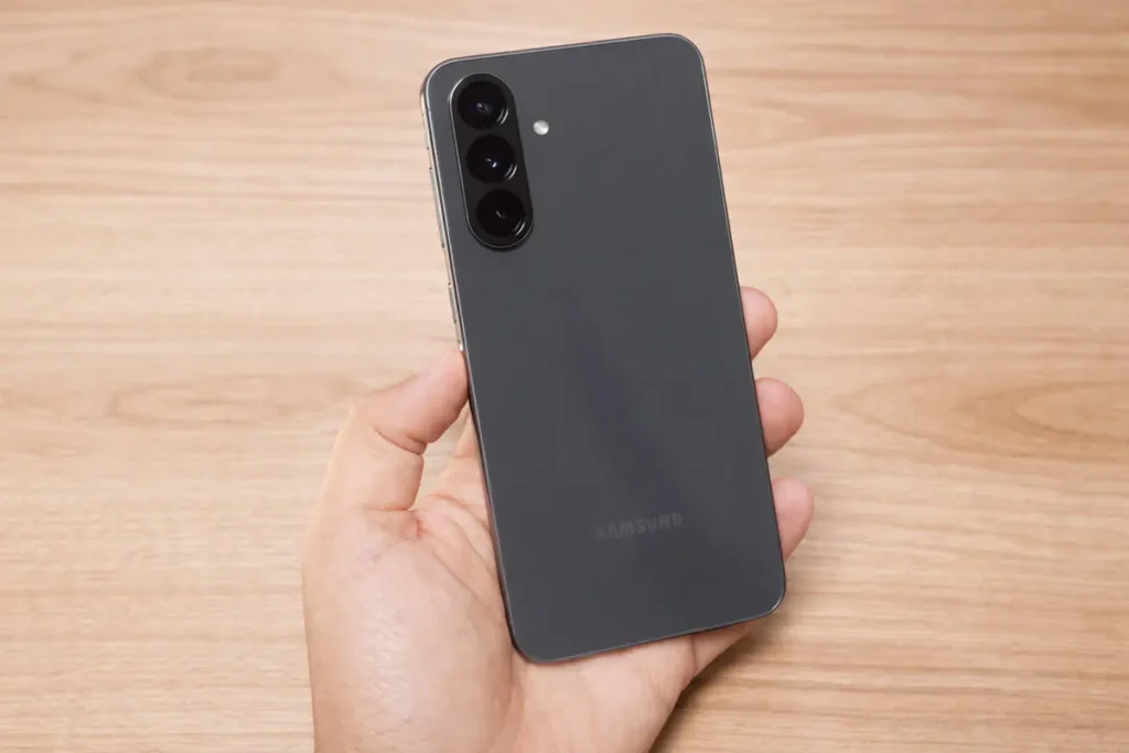 Celular Samsung Galaxy A56, cor cinza, em um fundo mesa de madeira em tons claros.
