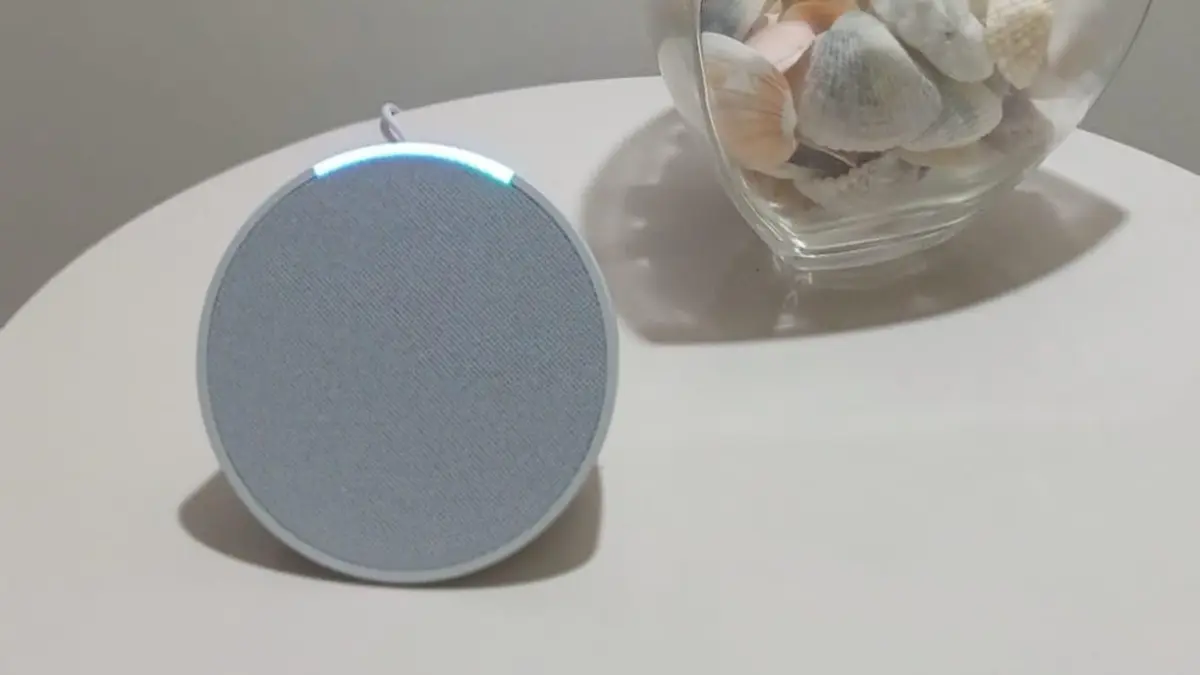 Assistente de voz com a Alexa Amazon Echo pop cor cinza com leds azuis sobe uma mesa branca.