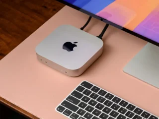 Apple Mac Mini sobe uma mesa de madeira com teclado e um tela.