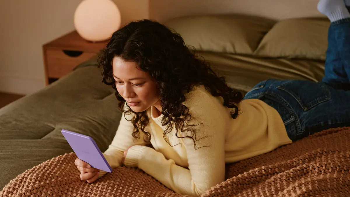Uma mulher deitada em uma cama com um Kindle 16 GB cor roxo.