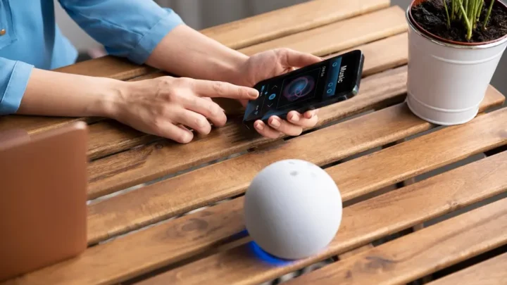 Assistente Virtual sobre uma mesa de madeira com uma mulher mexendo no smartphone.