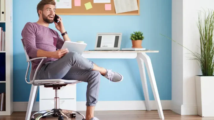 Uma pessoa sentada confortavelmente em um home office, segurando um tablet e falando ao telefone, cercada por uma decoração elegante.
