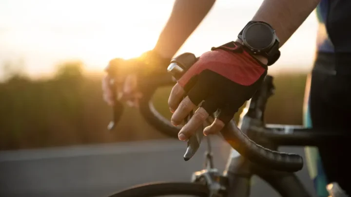 Braço de um homem segurando o guidão de uma bike de estrada usando luvas de ciclismo e um smartwtch. Smartwatch para ciclismo com GPS