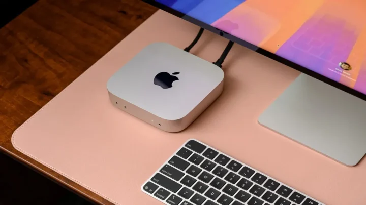 Apple Mac Mini sobe uma mesa de madeira com teclado e um tela.